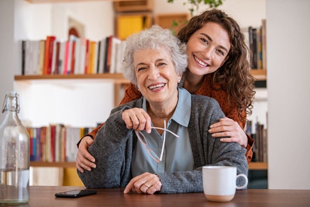 Young,Woman,Embracing,Senior,Mother,At,Home,And,Looking,At