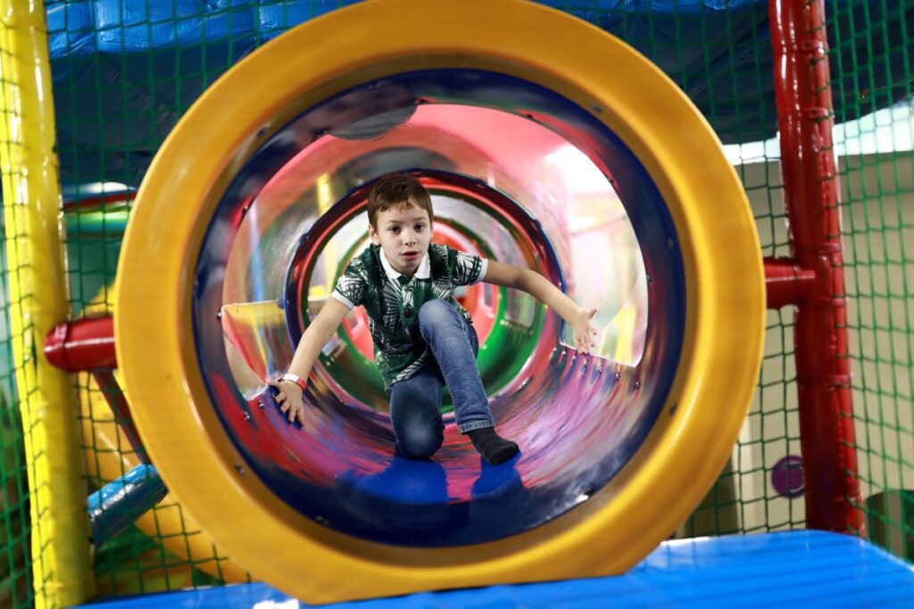 Kid,Sitting,In,Tube,On,Indoor,Playground