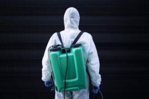 Man in white protective suit with reservoir for spraying and disinfection.