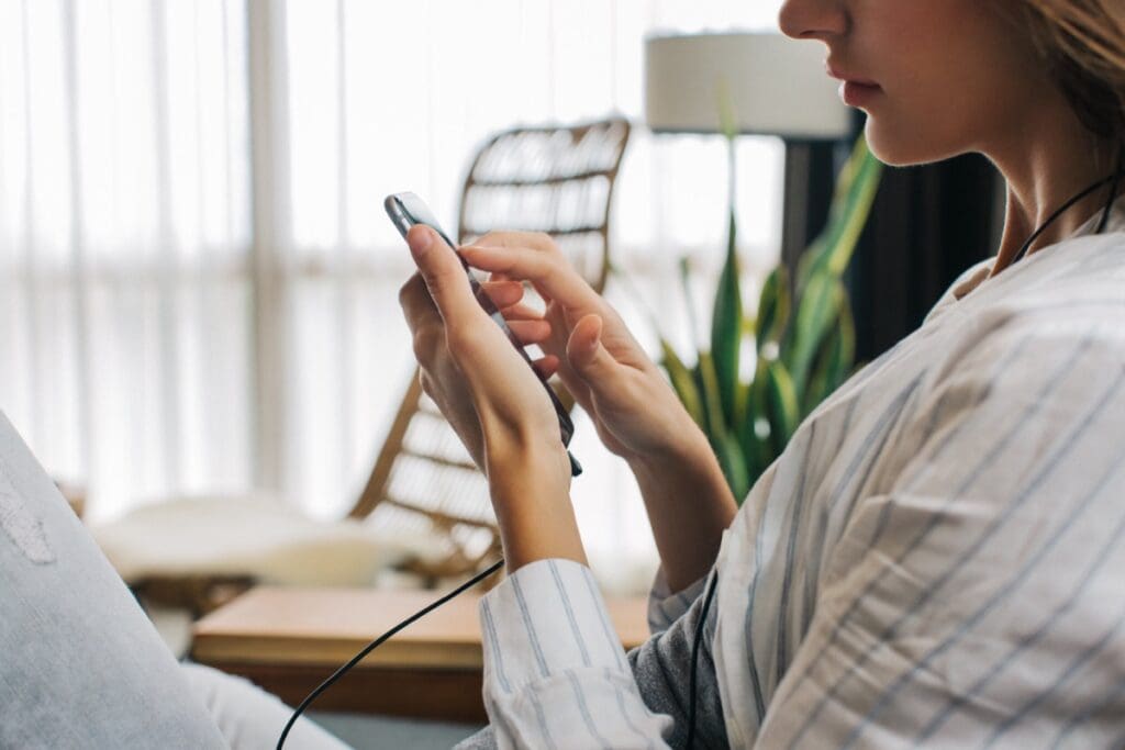 Closeup of Young Woman Sitting on Sofa and Using Touch Screen on Cellphone